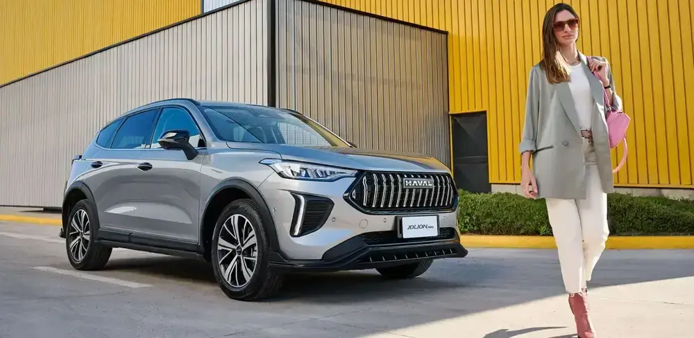 SUV hibrido GWM Jolion Pro HEV color plateado con una mujer caminando frente a el.